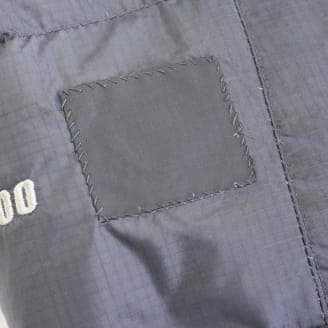 修理後の同じ黒い生地のクローズアップ画像。四角い補修用の布が縫い付けられており、穴が補修されている。