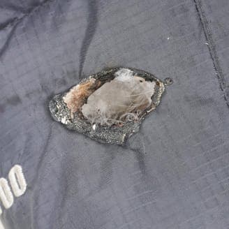 黒い生地に大きな穴があり、焦げたような跡が見えているクローズアップ画像。