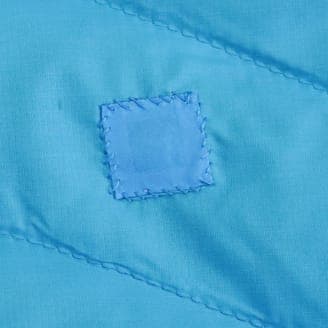 修理後の同じ青色の生地のクローズアップ画像。割け目が補修されており、四角い補修用の布が縫い付けられている。